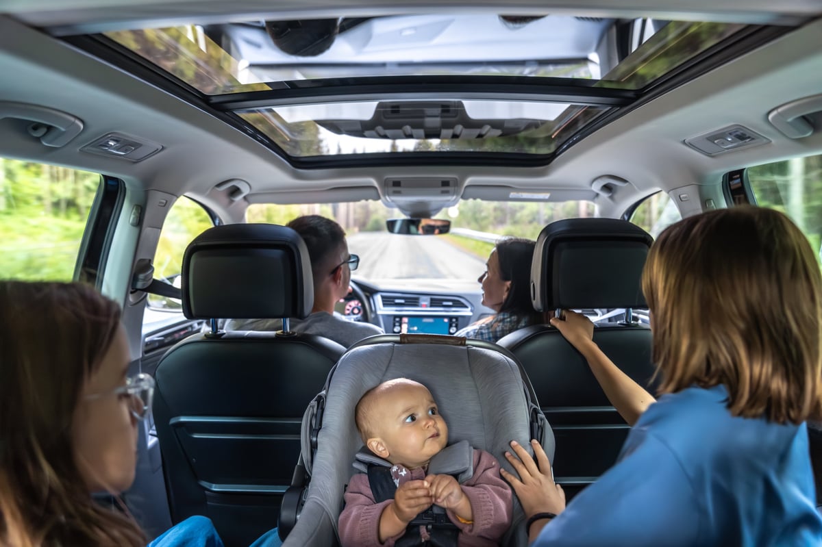 Steady backseat frame of a modern car. The baby watches the sister with curiosity, highlighting safety, comfort and an everyday family style on the journey.