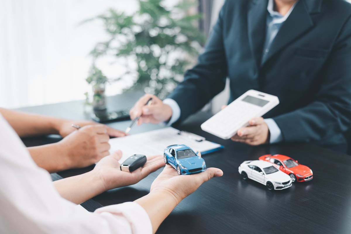 Businessman explaining car loan agreement with calculator, customer discussing auto finance deal at office desk with toy car and document, concept of vehicle loan, insurance or car leasing.