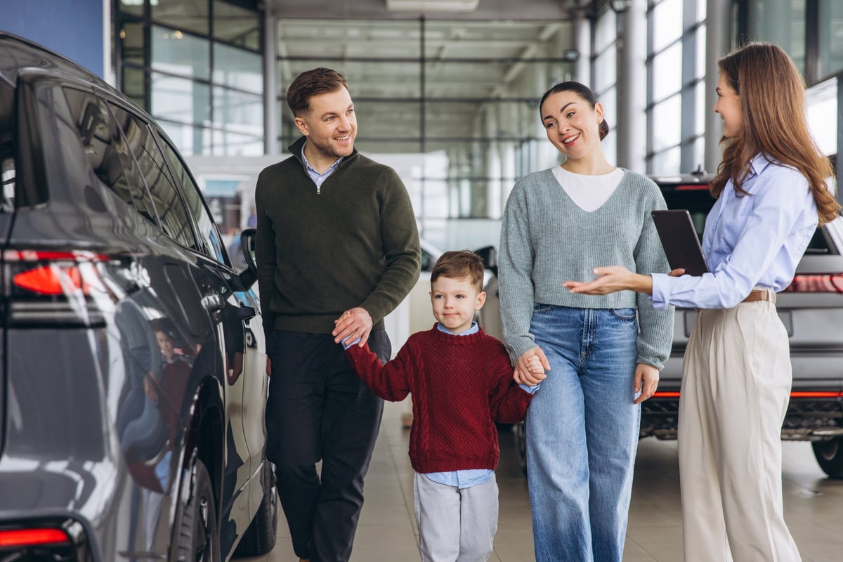 Happy family, including parents and son, interacting with a saleswoman at a car dealership, looking at vehicles