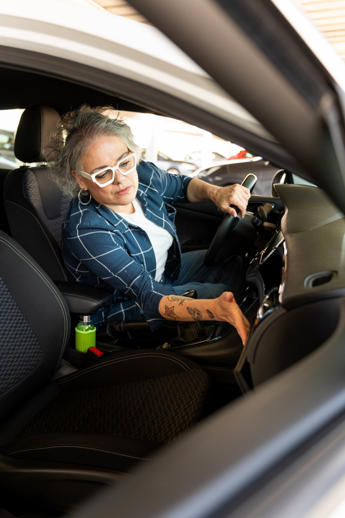 Mature adult woman with tattooed arm trying out a new car, preparing for a test drive