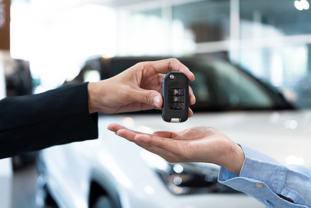 Close-up of car dealer handing over a key to a customer in a showroom. Successful vehicle purchase and ownership transfer. Automotive sales concept.