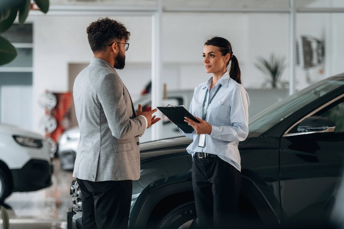Holding notepad with information. Business consultation between car dealer and buyer in showroom.