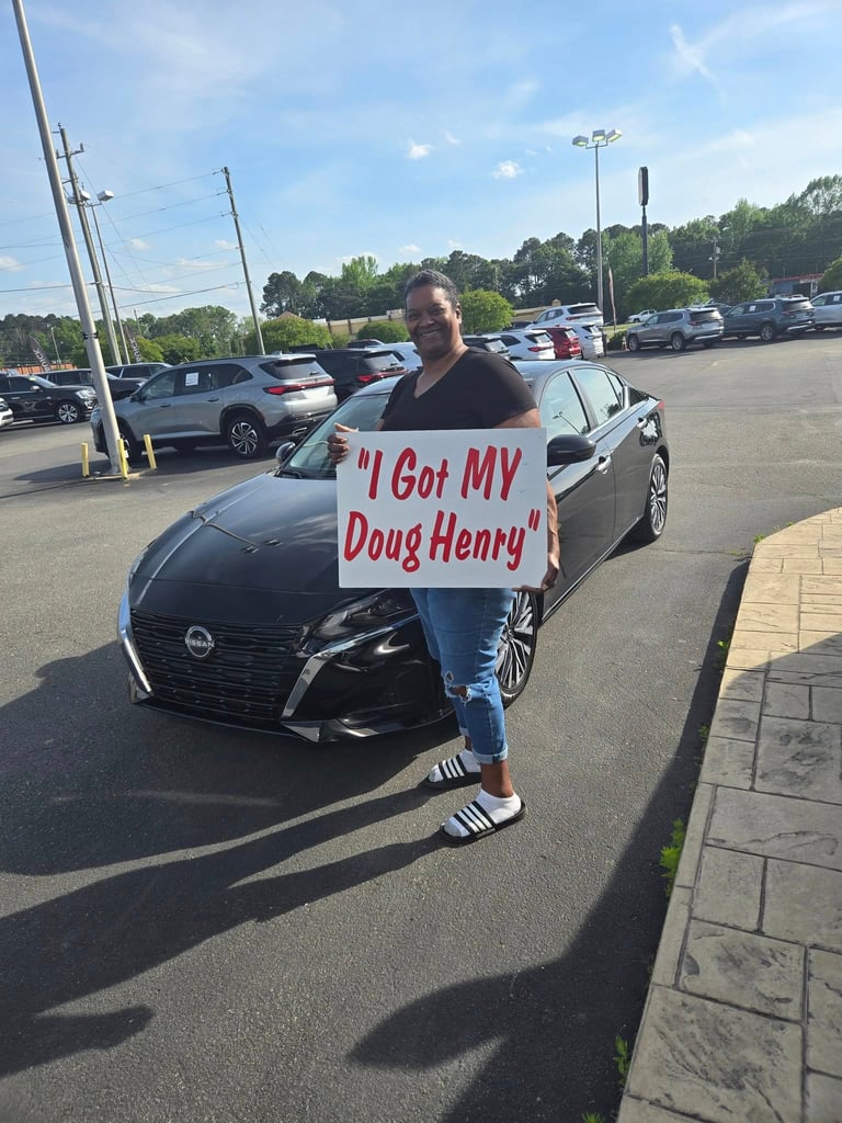 Person holding a sign reading I Got MY Doug Henry next to a black Nissan in a parking lot