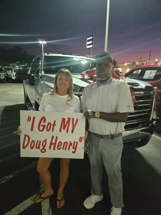 Woman and man at car dealership holding sign that reads I Got MY Doug Henry