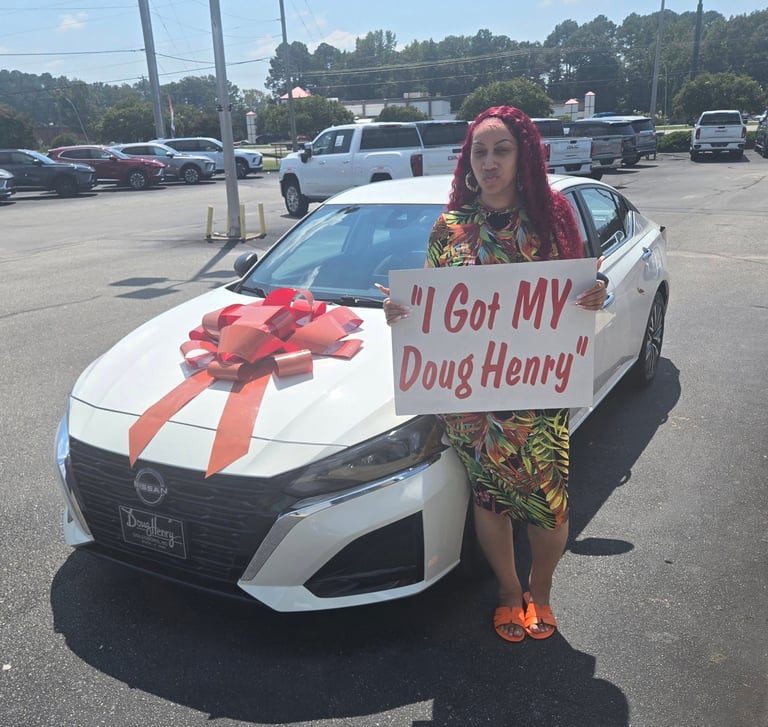 Woman with red hair standing next to white car with red bow and sign reading I Got MY Doug Henry