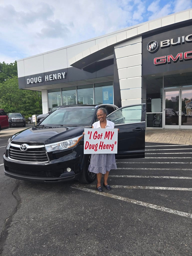 Woman holding I Got My Doug Henry sign in front of black Toyota vehicle at Doug Henry Buick GMC dealership