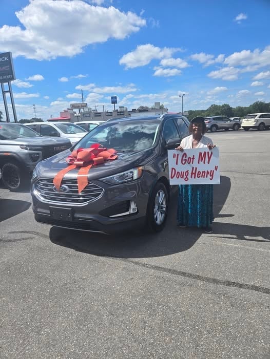 Woman holding I Got My Doug Henry sign next to new black Chevy Equinox with red bow in dealership lot