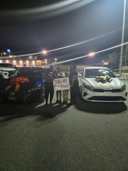 Group of people standing between vehicles at night holding a sign that reads I Got MY Power Upper