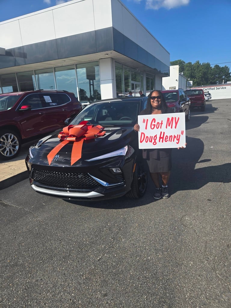 Woman holding sign I Got MY Doug Henry next to black car with large red bow at dealership
