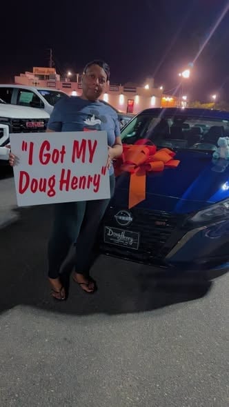 Man holding sign that says I Got MY Doug Henry standing next to a blue car with a red bow at night in a parking lot