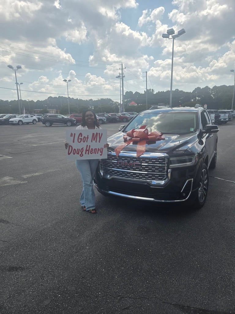 Woman holding sign that reads I Got MY Doug Henry standing next to a black SUV with red bow in parking lot
