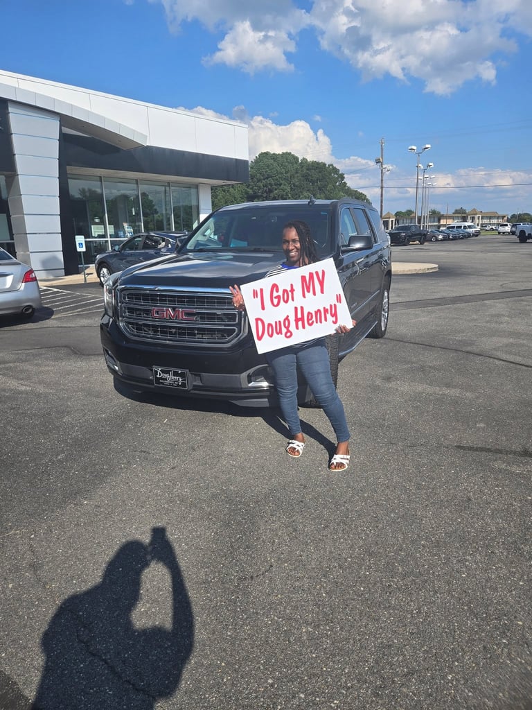 Woman holding I Got My Doug Henry sign in front of black GMC truck at dealership parking lot