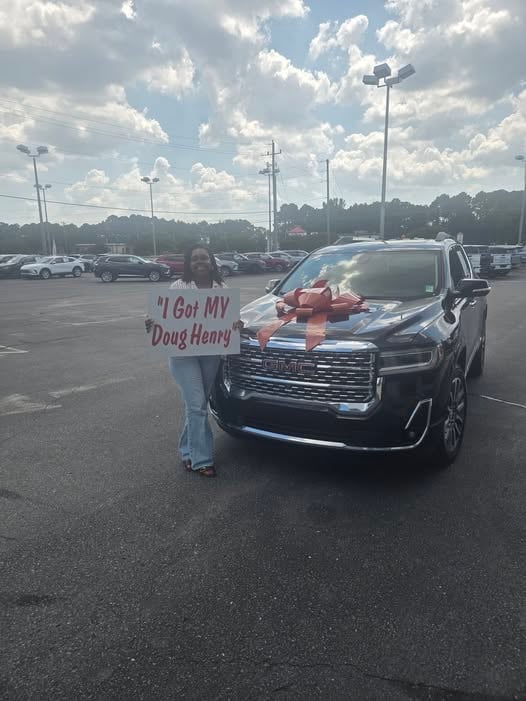 Woman holding I Got MY Doug Henry sign next to a black pickup truck with red bow in parking lot