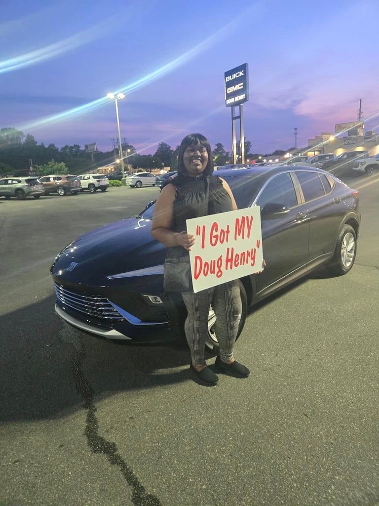 Person in dark clothing holding a sign reading I Got MY Doug Henry standing next to a black SUV in a parking lot at dusk