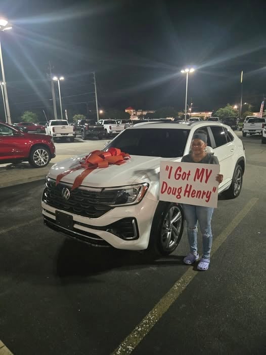 Person holding sign next to white Volkswagen with red bow in night parking lot