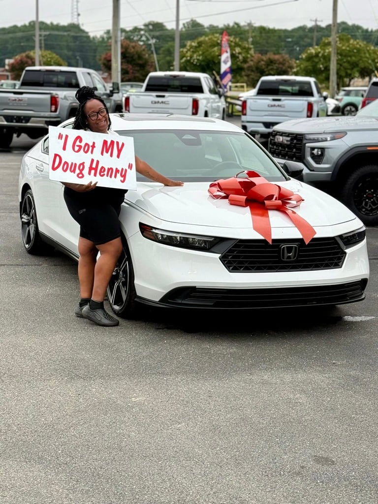 Woman holding sign next to new white Honda car with red bow in dealer lot