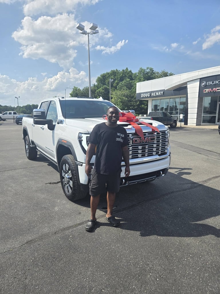 Man posing next to new white GMC pickup truck with red bow at dealership lot